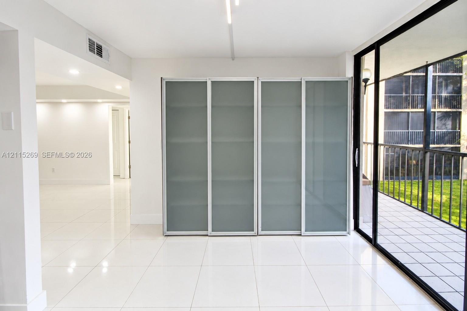 Built-in floor-to-ceiling cabinetry with frosted glass panels, expansive tile flooring, and large sliding glass doors opening to a tiled balcony