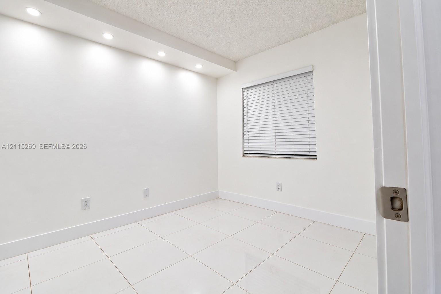 Room featuring large-format ceramic tile flooring, recessed cove lighting, and a single window with horizontal blinds