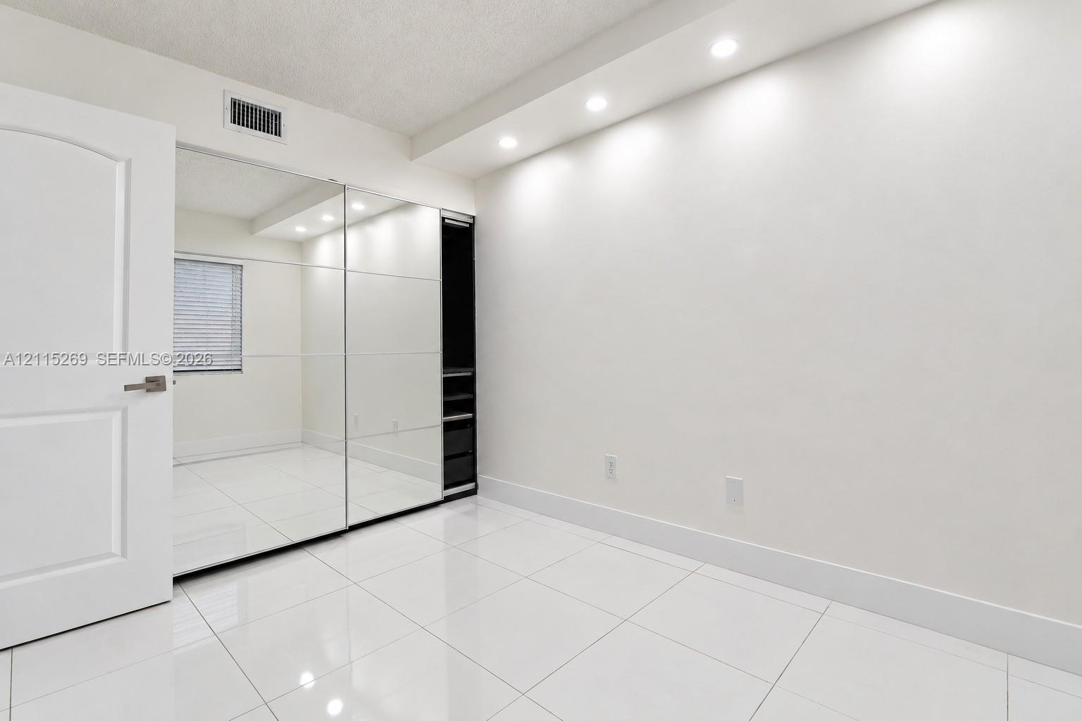 Wall-to-wall mirrored closet doors, recessed ceiling lighting, glossy tiled flooring, and built-in closet shelving