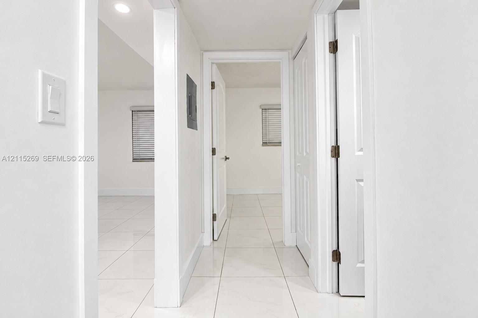 Neutral-toned interior featuring large-format ceramic tile flooring, recessed lighting, white six-panel doors, and white-framed windows with horizontal blinds