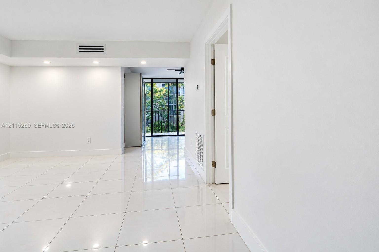 Glossy white tile flooring, recessed ceiling lighting, and floor-to-ceiling glass-paneled sliding doors