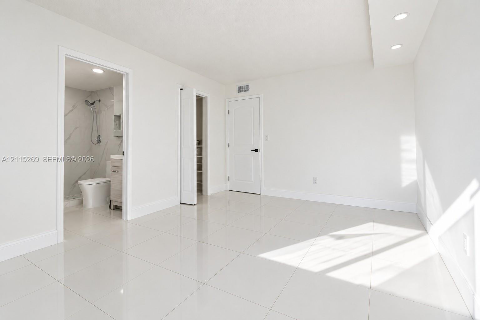 Interior space featuring large-format tile flooring, recessed ceiling lighting, a dedicated closet with a folding door, and an attached bathroom with a walk-in shower