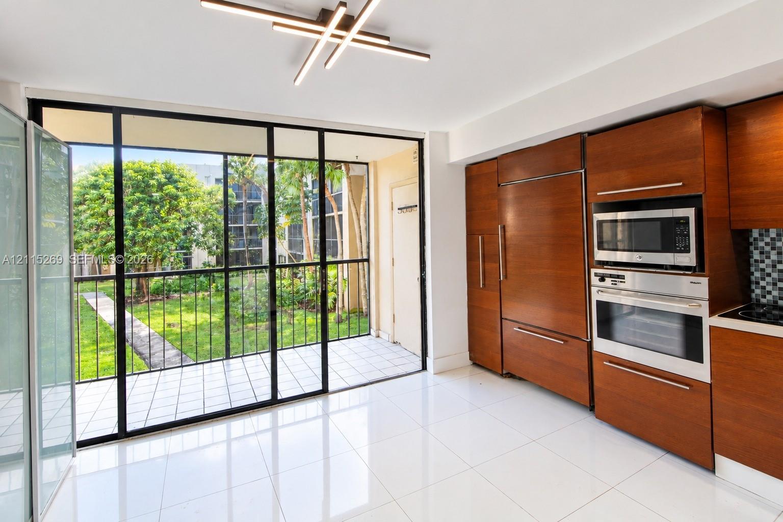 Kitchen featuring wood-veneer cabinetry, integrated refrigerator, built-in wall oven and microwave, ceramic tile flooring, and floor-to-ceiling glass panel door opening to a tiled balcony