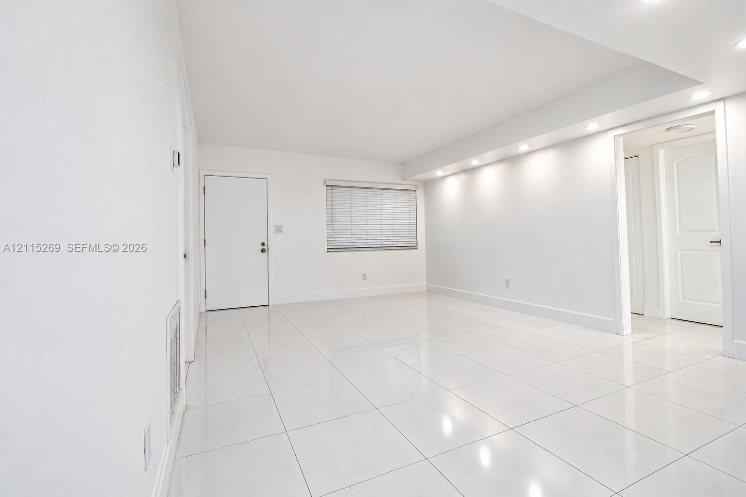 Interior space featuring high-gloss tile flooring, recessed ceiling lighting, smooth white walls, and a recessed window with horizontal blinds