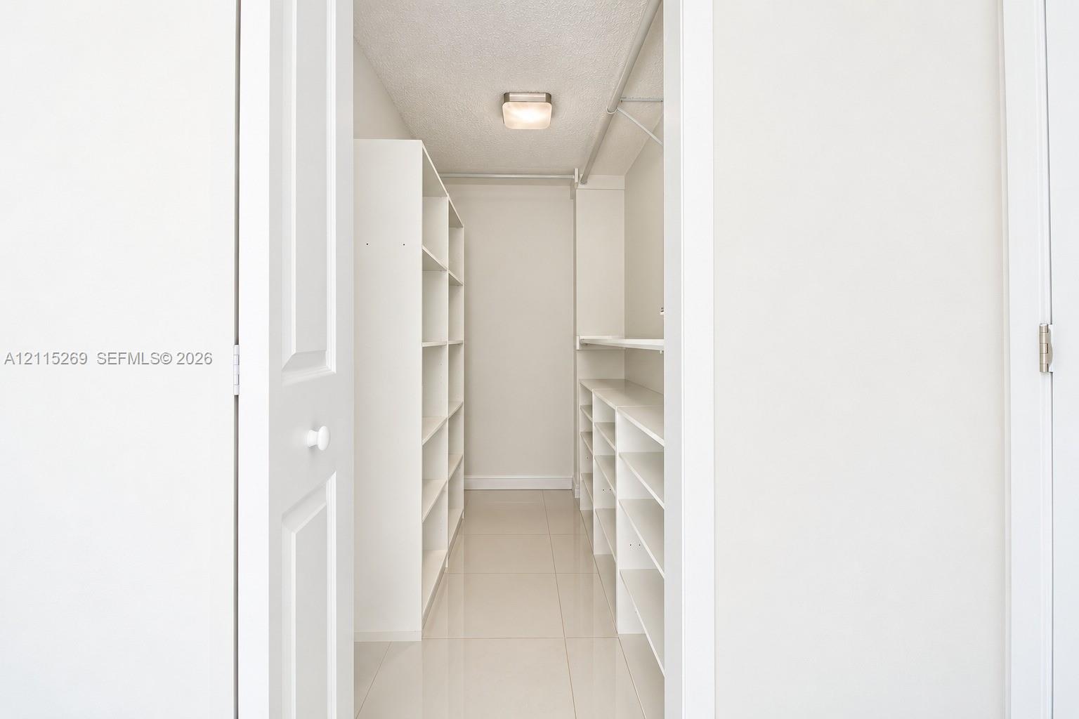 Walk-in closet featuring white built-in shelving, tile flooring, and a flush-mount ceiling light fixture