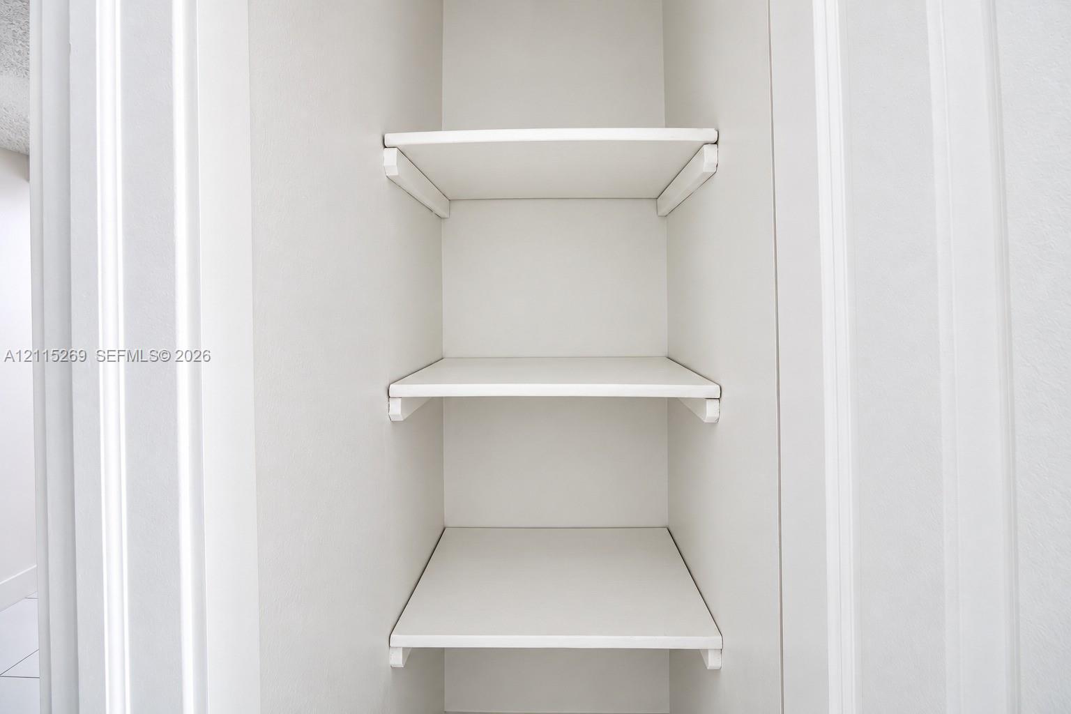 Built-in storage closet featuring three fixed white shelves and bracket supports