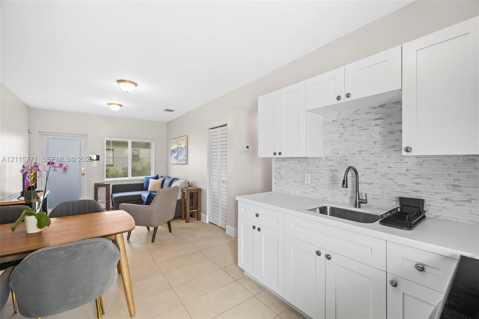 Kitchen featuring white shaker-style cabinetry, a textured stone-finish backsplash, a stainless steel undermount sink with a gooseneck faucet, and light-toned tile flooring