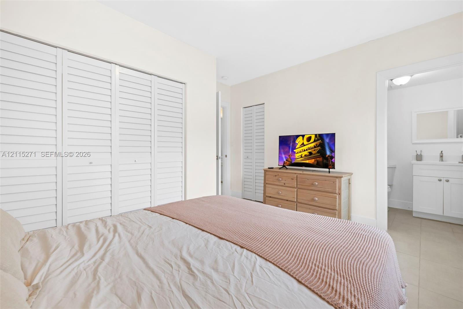 Room featuring large-scale closet storage with white louvered doors, tile flooring, and a crisp neutral color palette