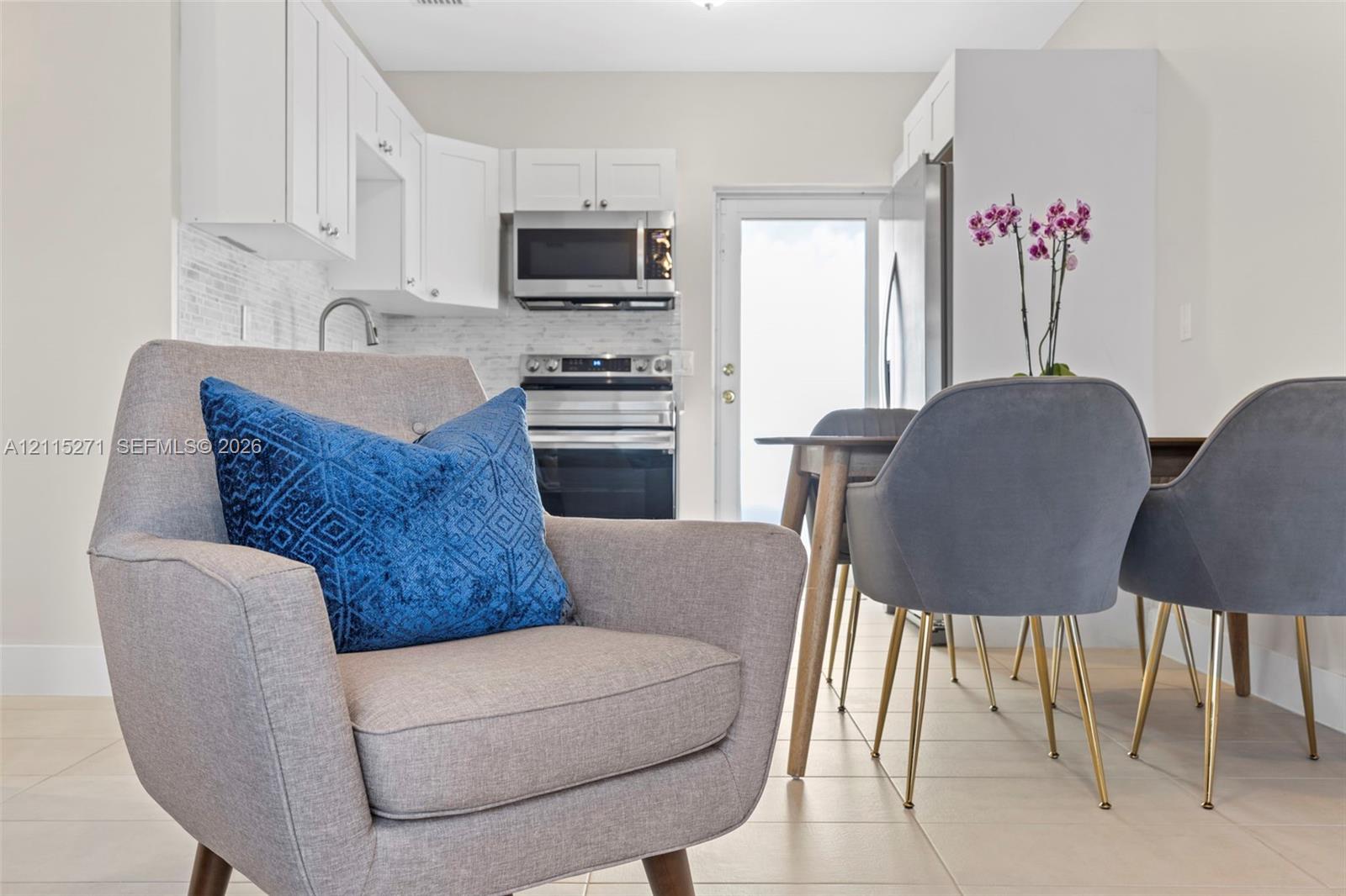 Kitchen featuring white shaker-style cabinetry, a stone-finish backsplash, stainless steel appliances, and tile flooring