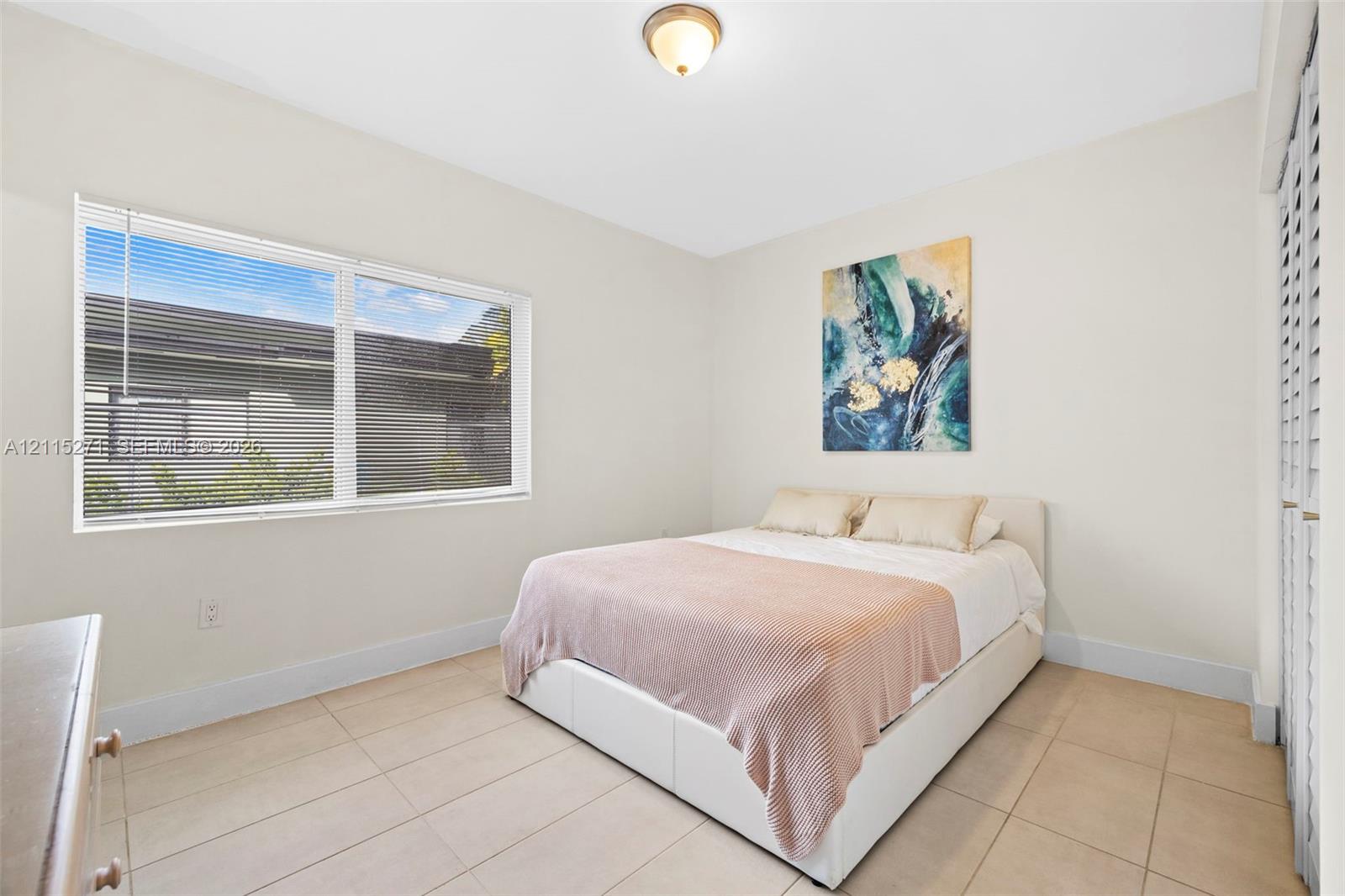 Neutral-toned interior space featuring light-colored tile flooring, a large horizontal window, flush-mount ceiling lighting, and louvered closet doors