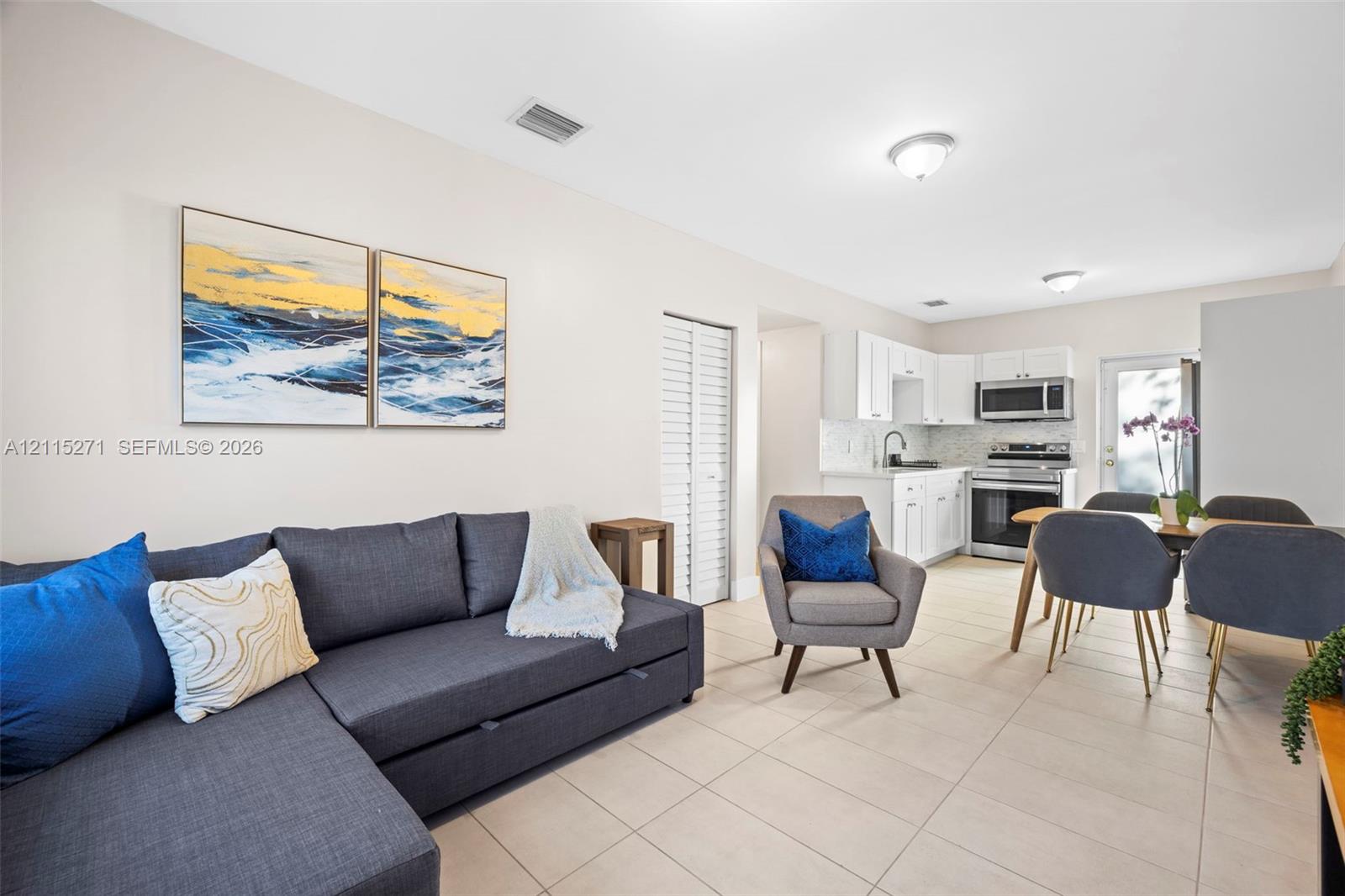 Kitchen area featuring white cabinetry, a tiled backsplash, and stainless steel appliances, all set atop neutral tile flooring