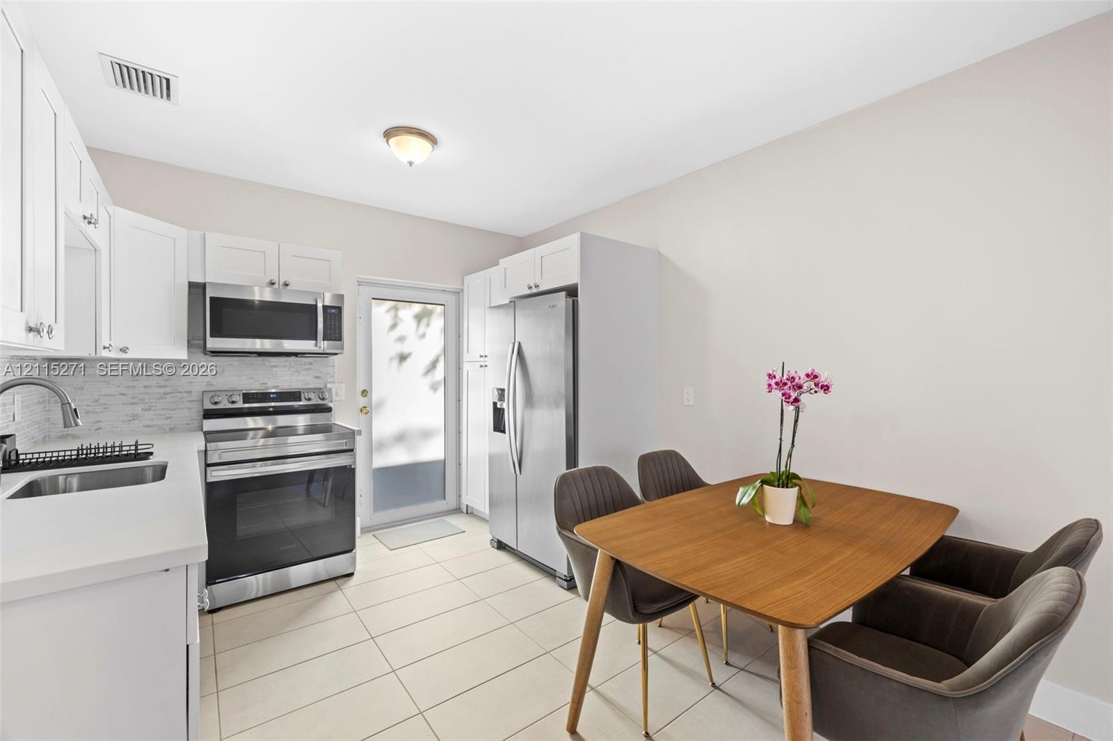 Kitchen featuring white cabinetry, solid-surface countertops, tile backsplash, stainless steel appliances, and tile flooring