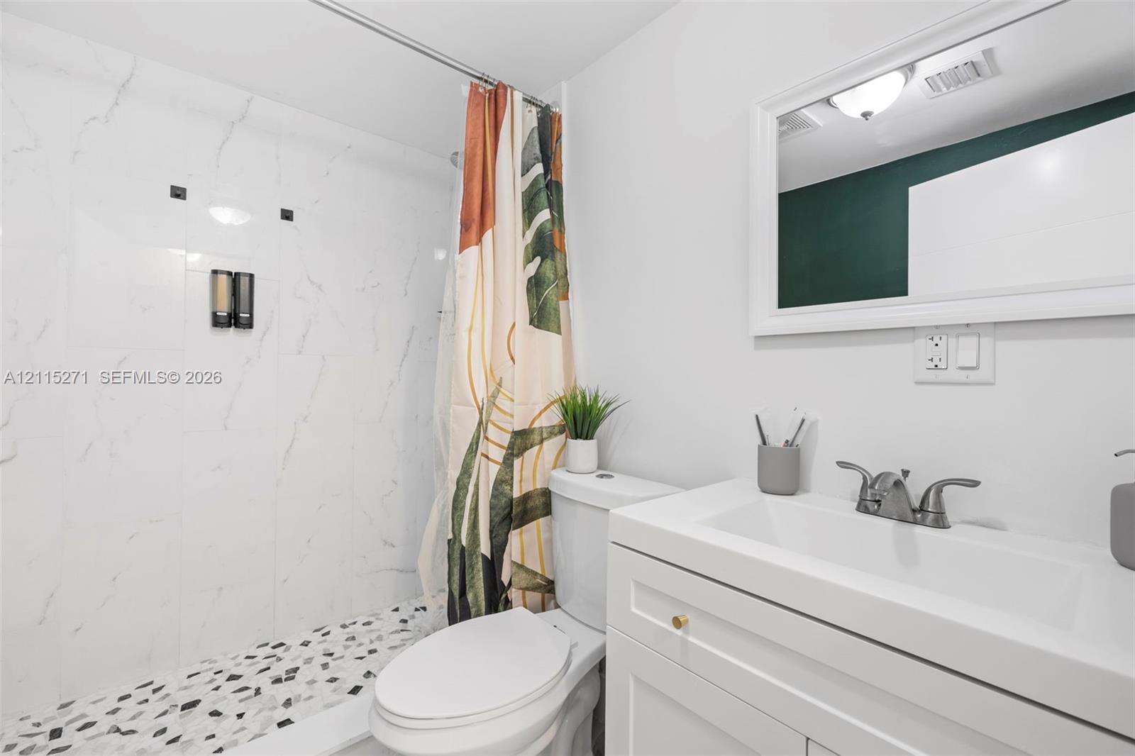Bathroom featuring a white vanity with a rectangular sink, stone-patterned shower wall tile, pebble-style shower floor, and a rectangular framed mirror