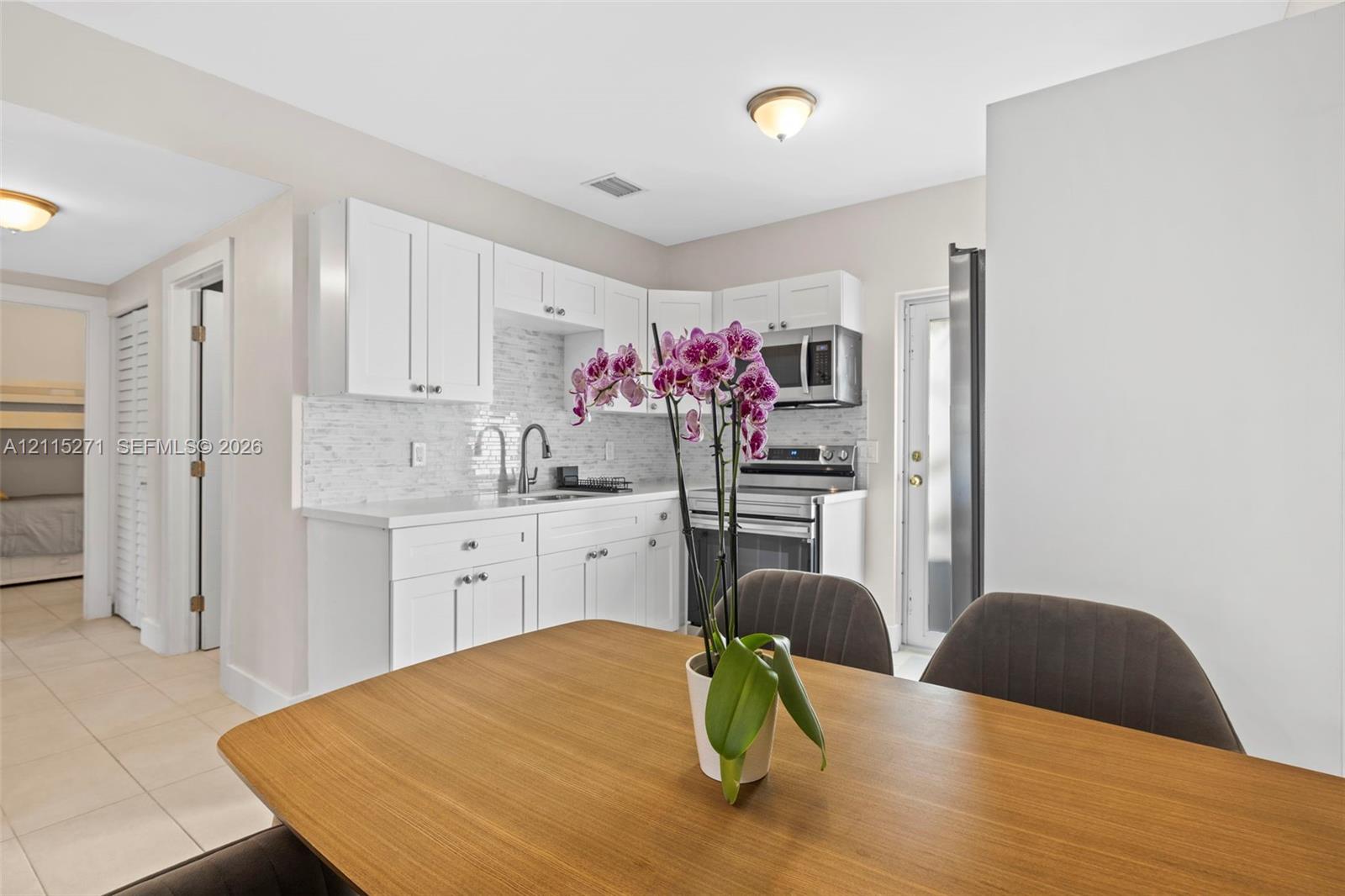 Kitchen featuring white shaker-style cabinetry, a light-toned stone-look tile backsplash, stainless steel appliances, and neutral tile flooring
