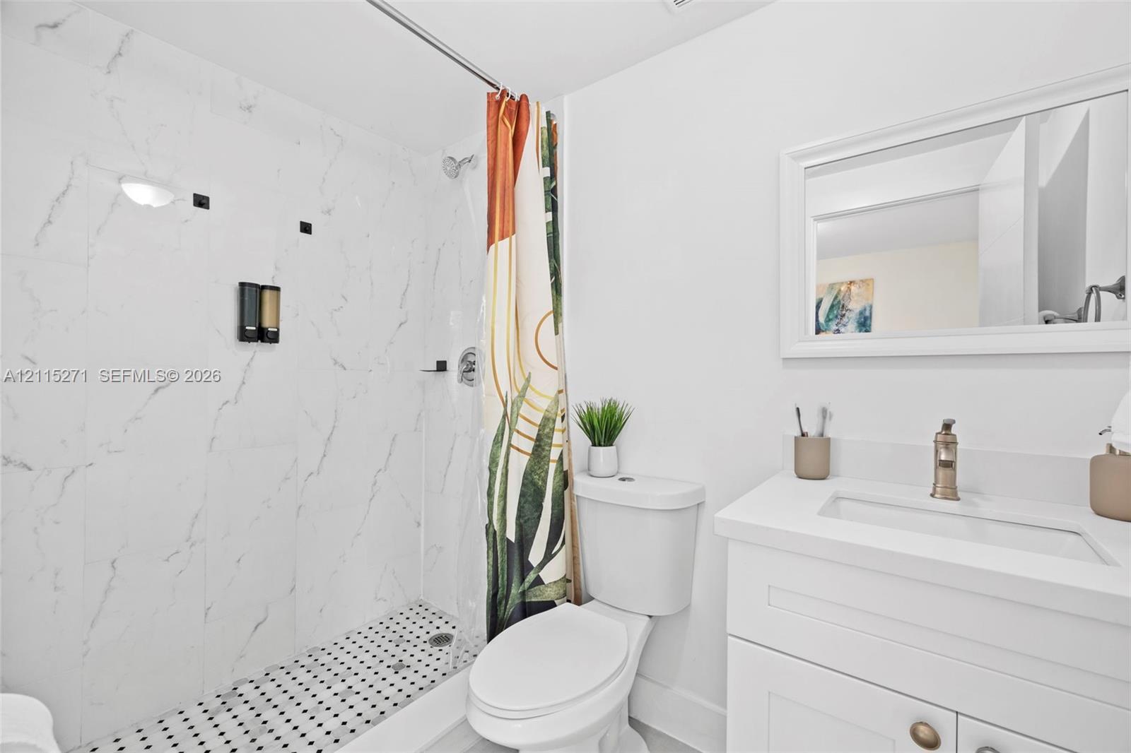 Bathroom featuring a walk-in shower with stone-patterned tile surround, penny-tile flooring, a vanity with a white countertop and integrated sink, and a framed wall mirror