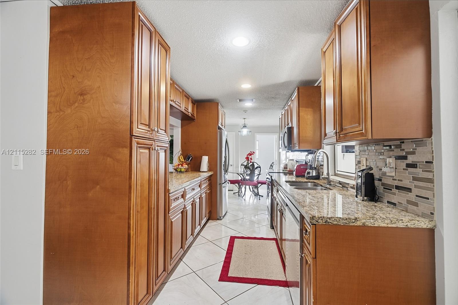 Kitchen featuring natural wood cabinetry, stone-patterned countertops, a decorative tile backsplash, recessed lighting, and tile flooring