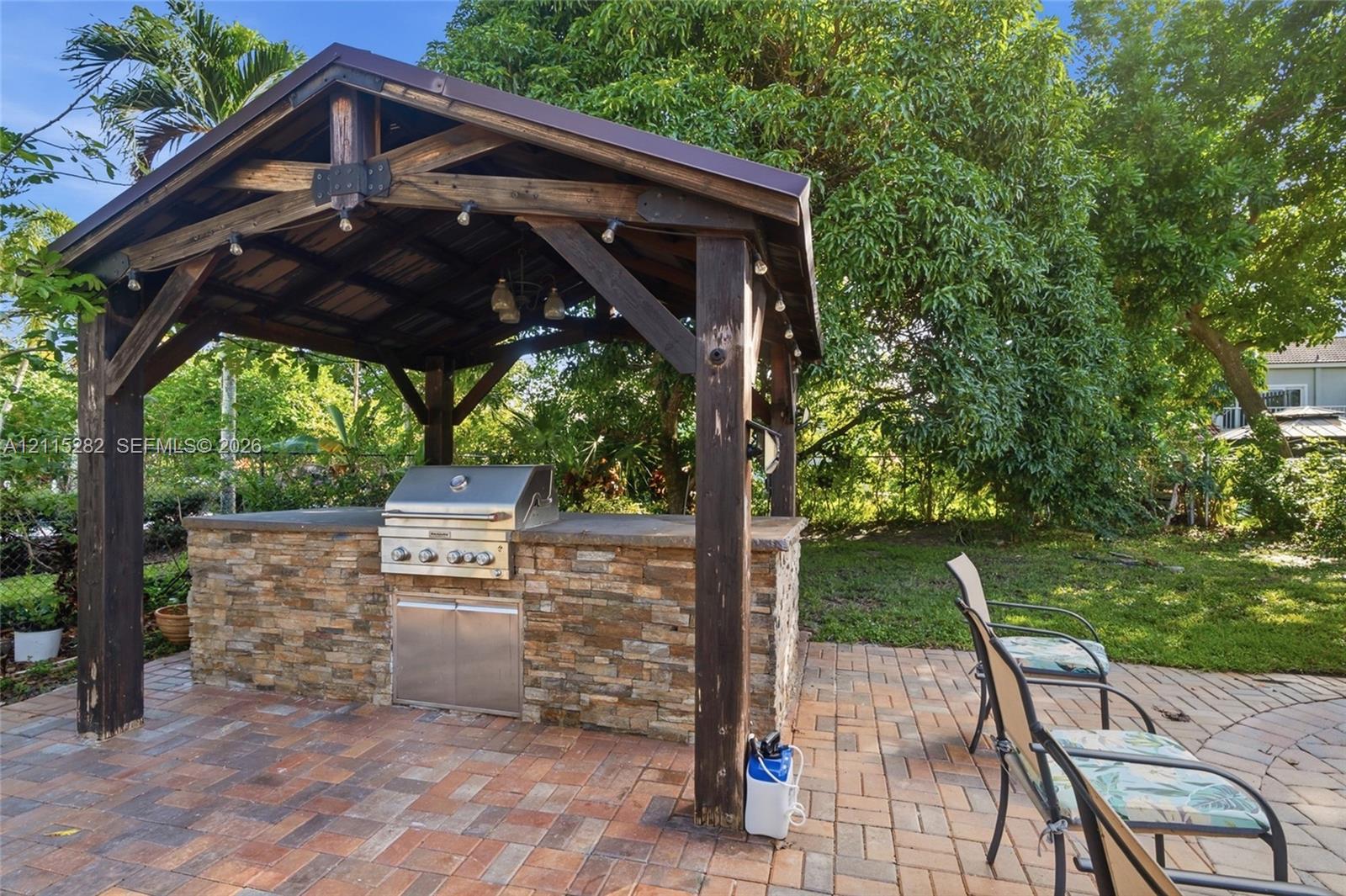 Timber-frame pavilion featuring a stacked-stone outdoor kitchen, stainless steel grill, and paver patio flooring