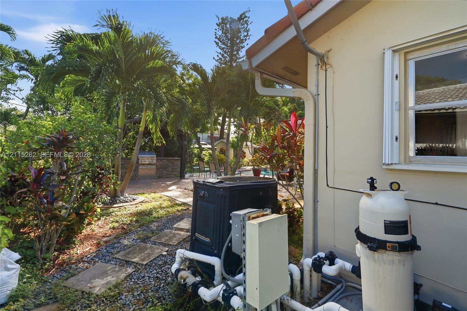 Exterior space featuring mature palms, stone-tiled path, and a masonry-clad outdoor kitchen structure