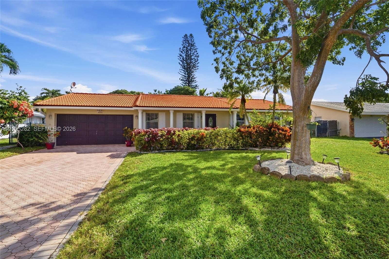 Single-story exterior featuring a terra cotta tile roof, covered front entryway with columns, paver driveway, and mature landscaping Single-story exterior featuring a terra cotta tile roof, covered front entryway with columns, paver driveway, and mature landscaping