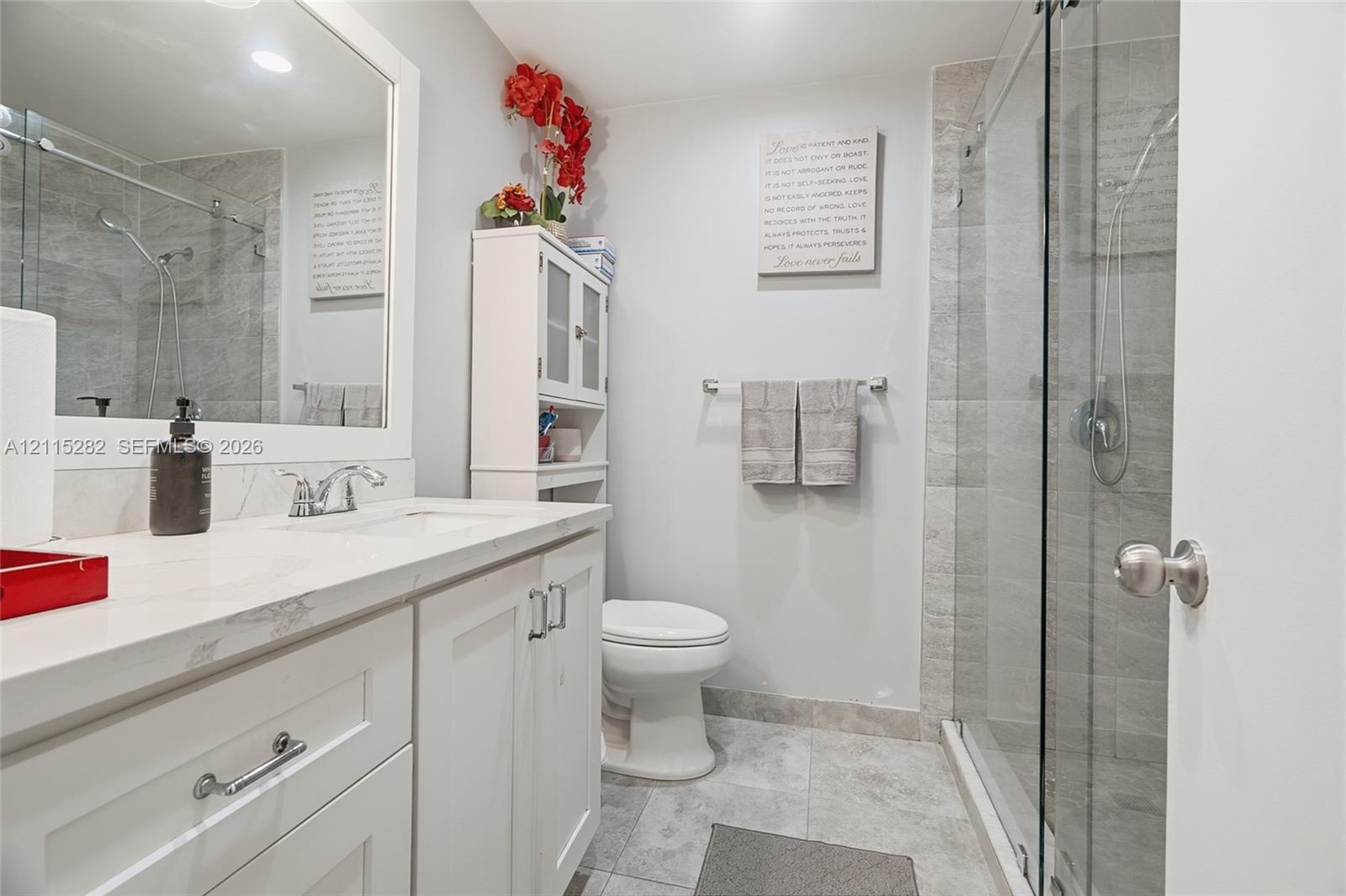 Bathroom featuring a white vanity with a solid-surface countertop, an integrated sink, a glass-enclosed shower with tiled surround, and tiled flooring