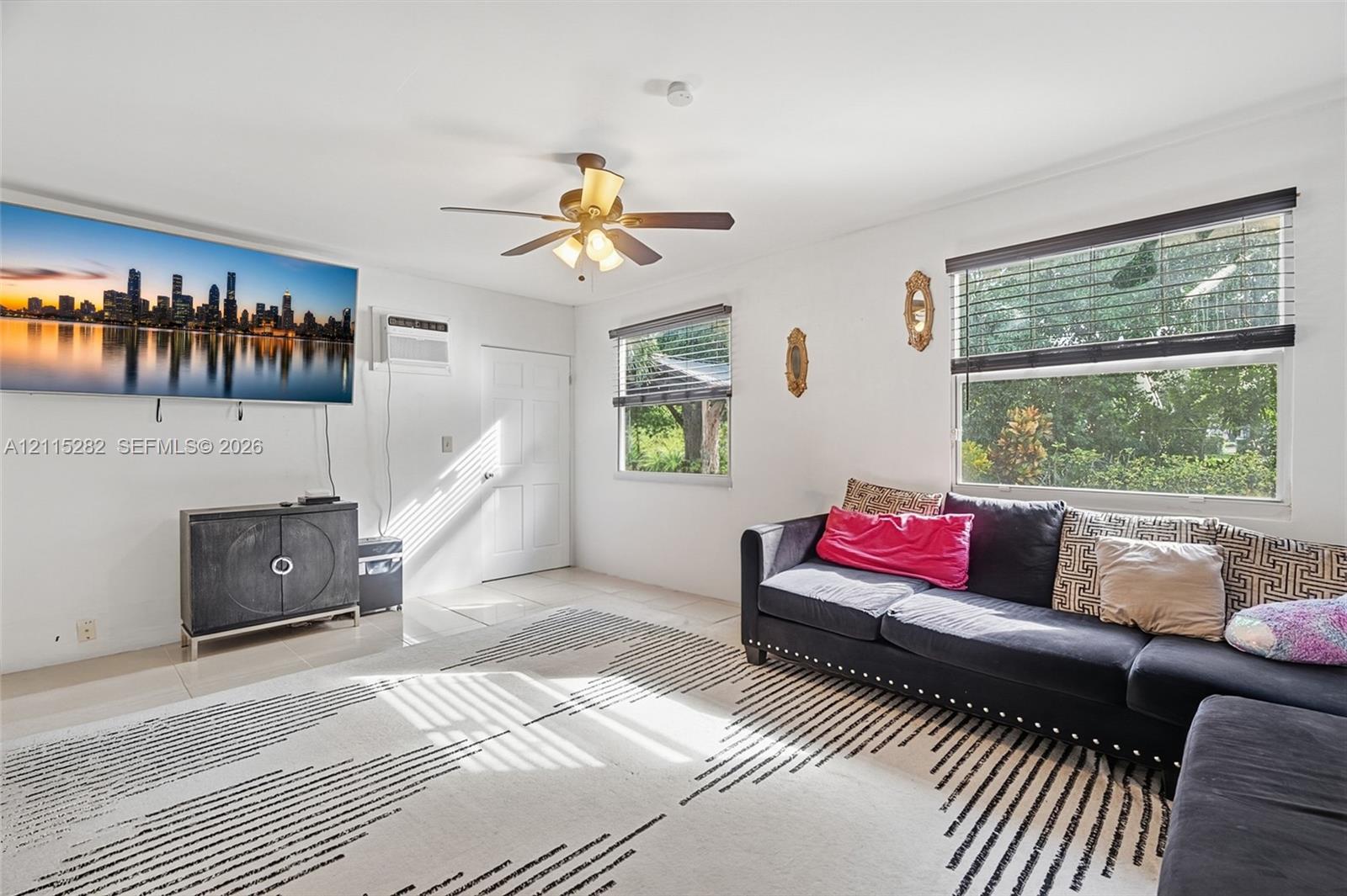 Living area featuring neutral tile flooring, a multi-blade ceiling fan with integrated lighting, and horizontal window blinds