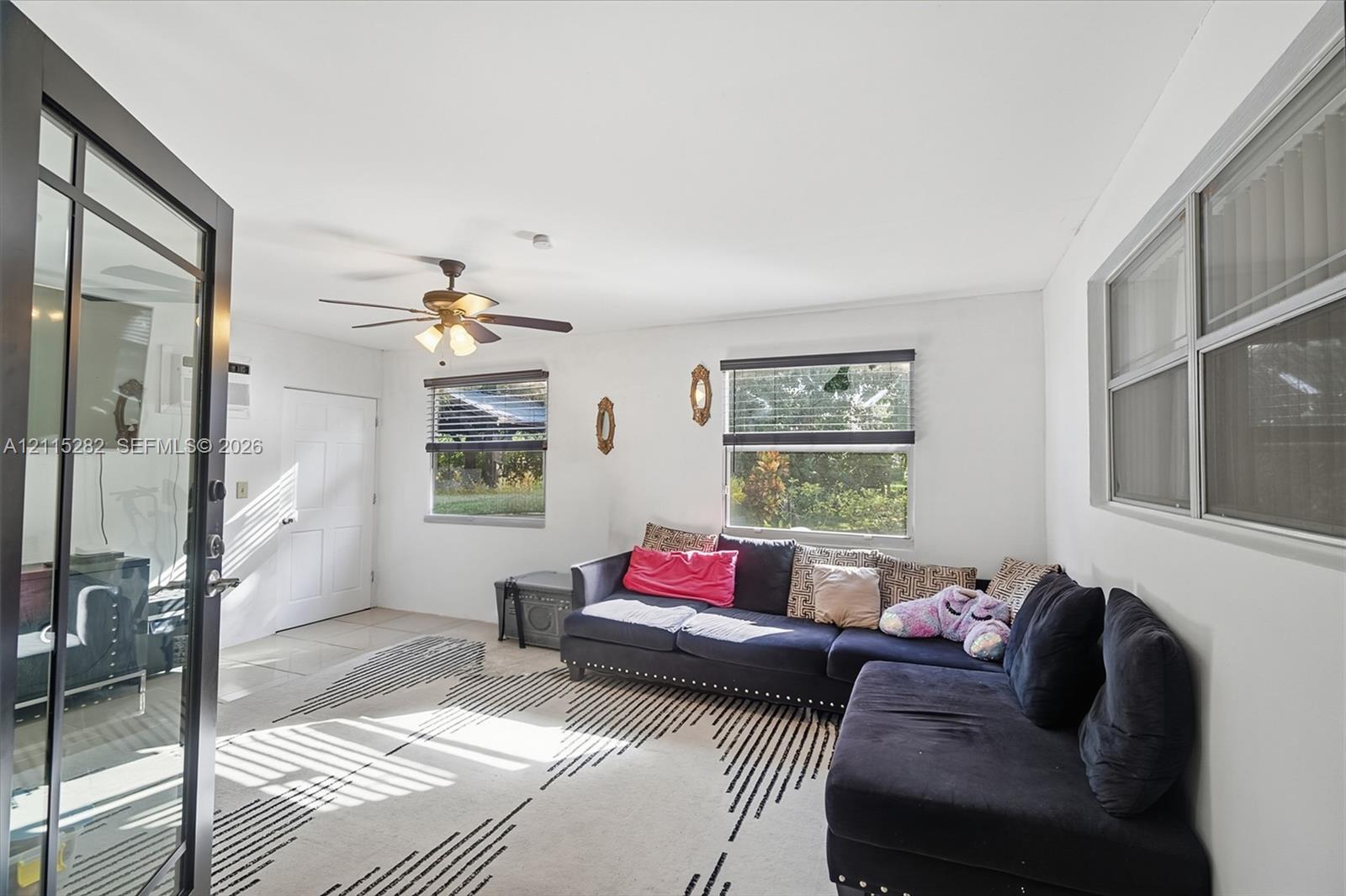 Living area featuring tile flooring, a multi-blade ceiling fan with integrated lighting, and multiple windows with horizontal blinds