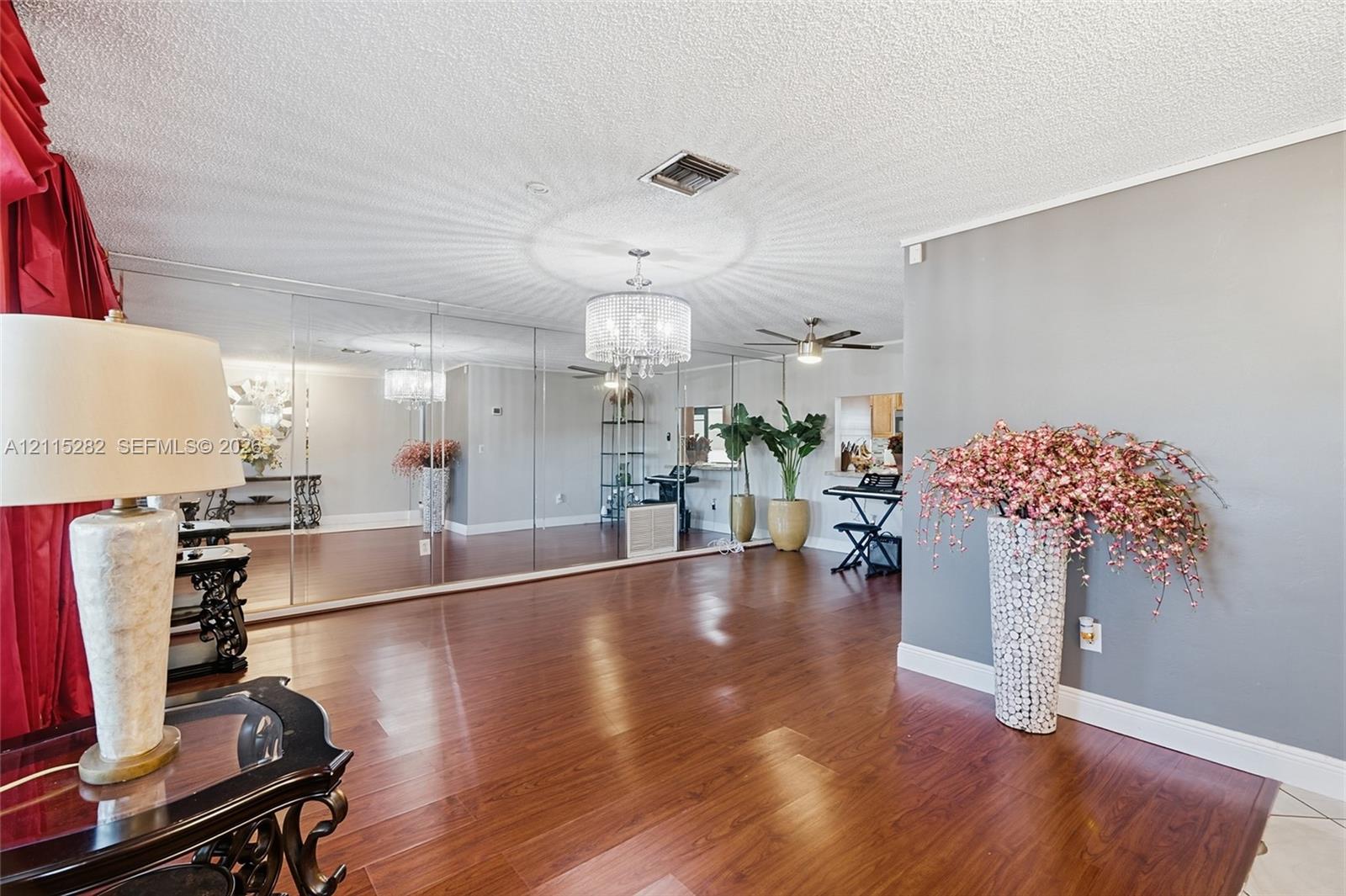 Open floor plan featuring wood-finish flooring, floor-to-ceiling mirror wall, and a multi-light drum chandelier Open floor plan featuring wood-finish flooring, floor-to-ceiling mirror wall, and a multi-light drum chandelier