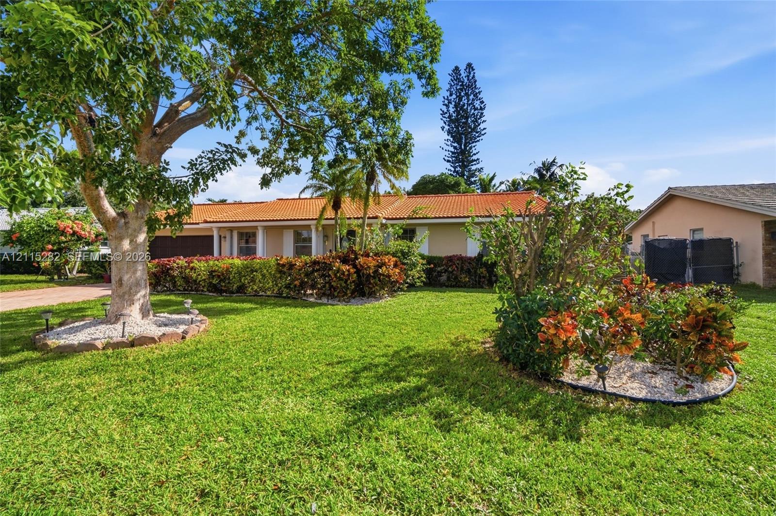 Single-story residence featuring a terracotta-tiled roof, manicured lawn, and established landscaping with mature trees Single-story residence featuring a terracotta-tiled roof, manicured lawn, and established landscaping with mature trees
