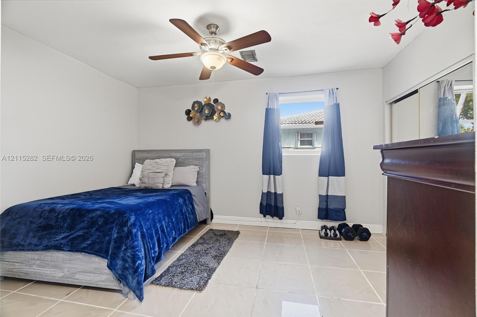 Room featuring light-toned tile flooring, neutral wall paint, a ceiling fan with integrated lighting, and a closet with sliding mirrored doors