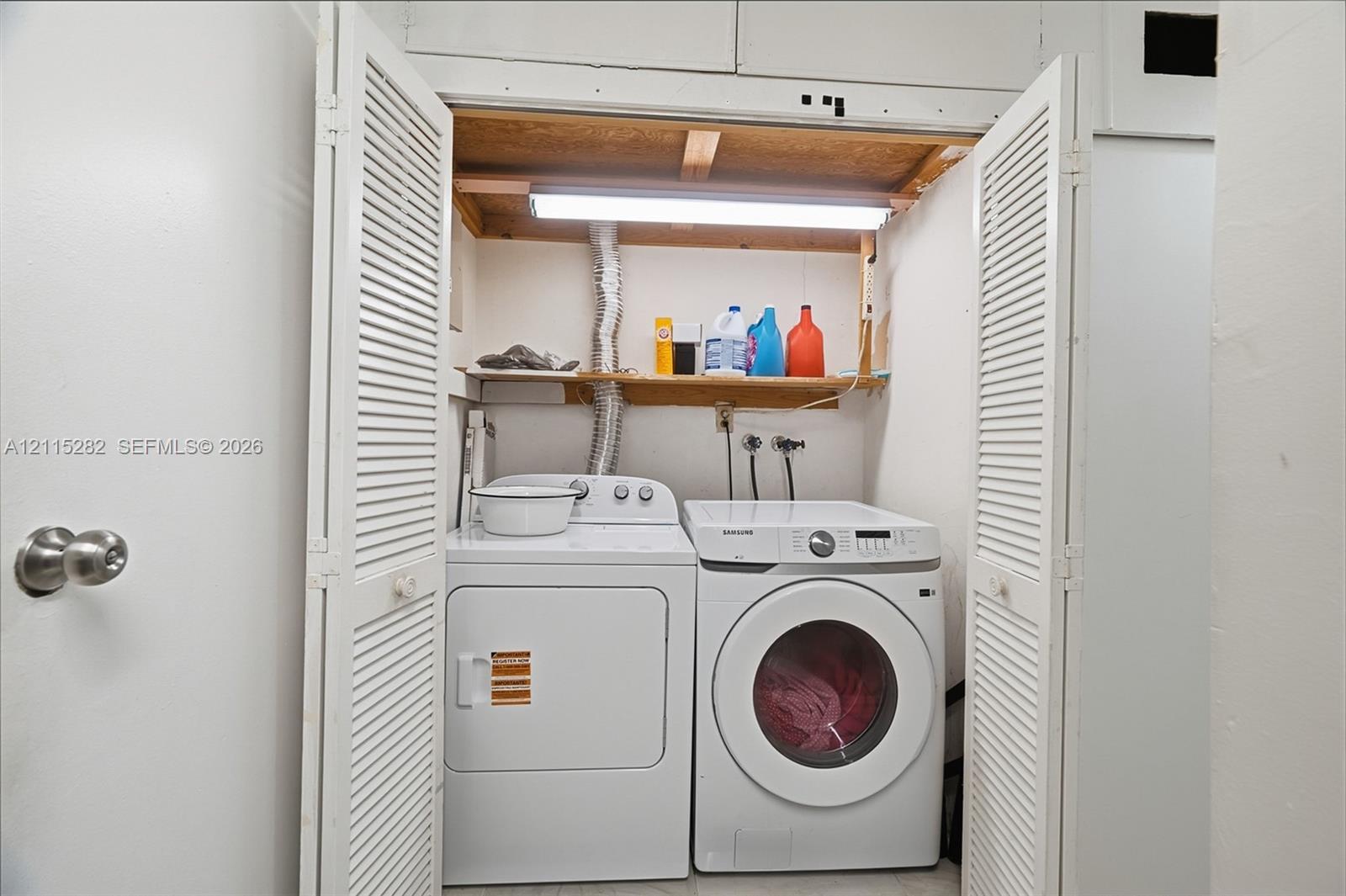 Laundry area featuring louvered bifold doors, overhead lighting, and built-in wooden shelving