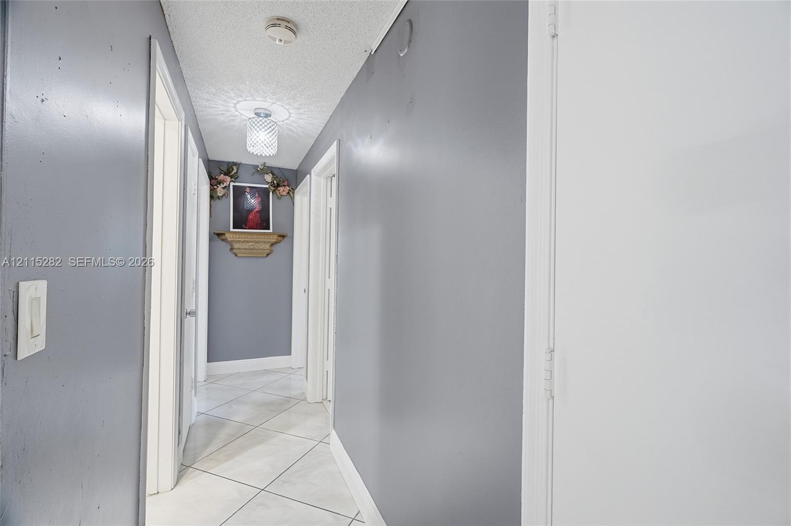 Neutral-toned hallway featuring large-format diagonal tile flooring, smooth-finish walls, and decorative ceiling-mounted lighting