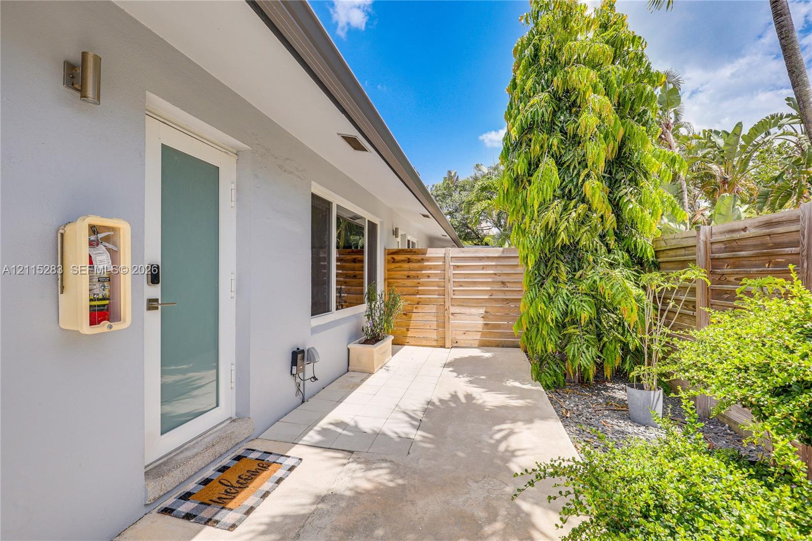 Exterior entry area featuring a glass-paneled door, concrete patio, horizontal wood slat privacy fencing, and stone landscape ground cover