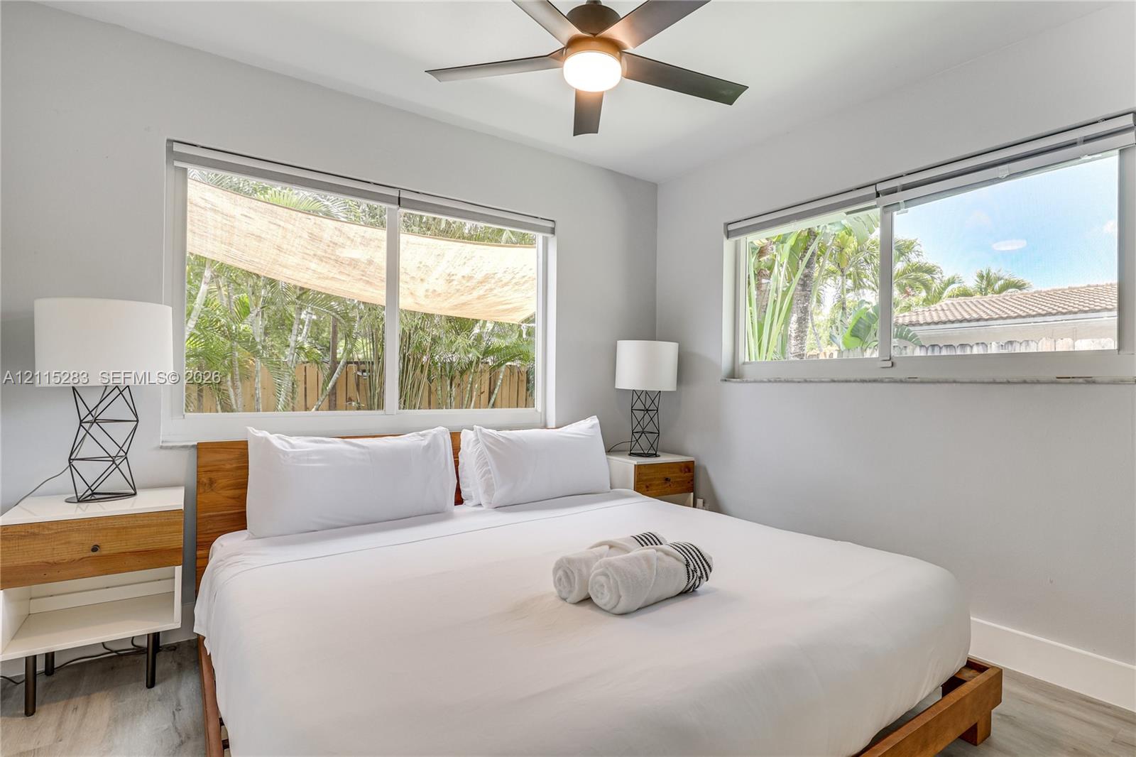 Neutral-toned bedroom featuring large windows, wood-finish flooring, and a ceiling fan with integrated lighting