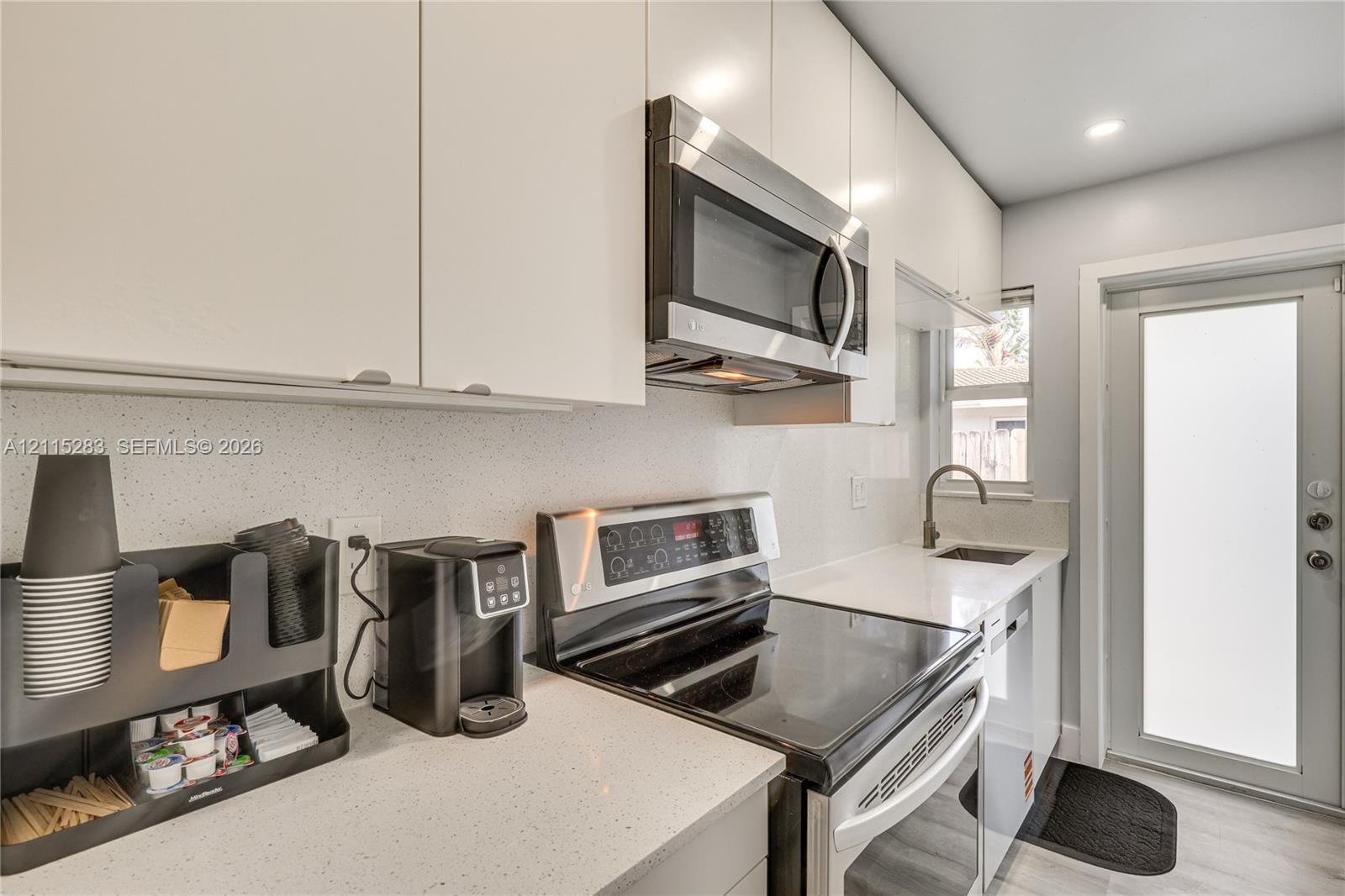 Kitchen featuring flat-panel white cabinetry, solid-surface countertops, stainless steel appliances, and a modern gooseneck faucet