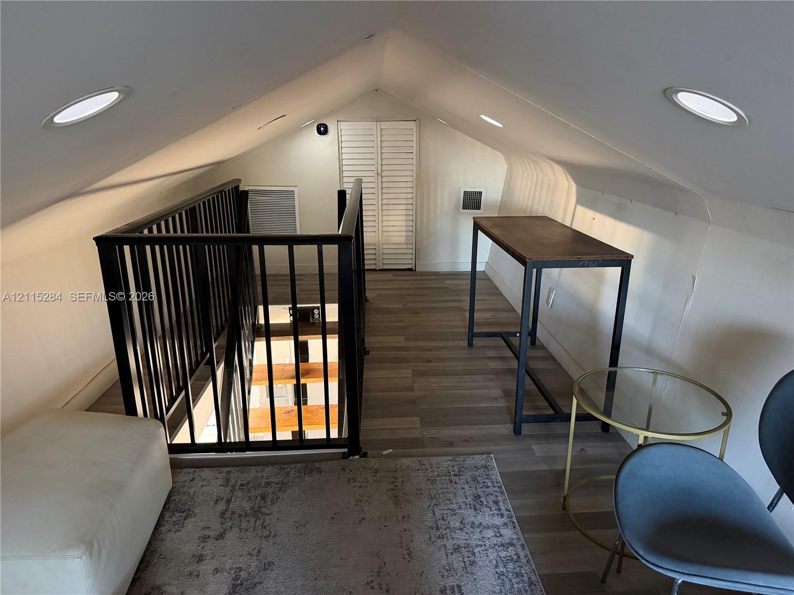 Vaulted ceiling with recessed lighting, wood-finish flooring, and black metal staircase railing