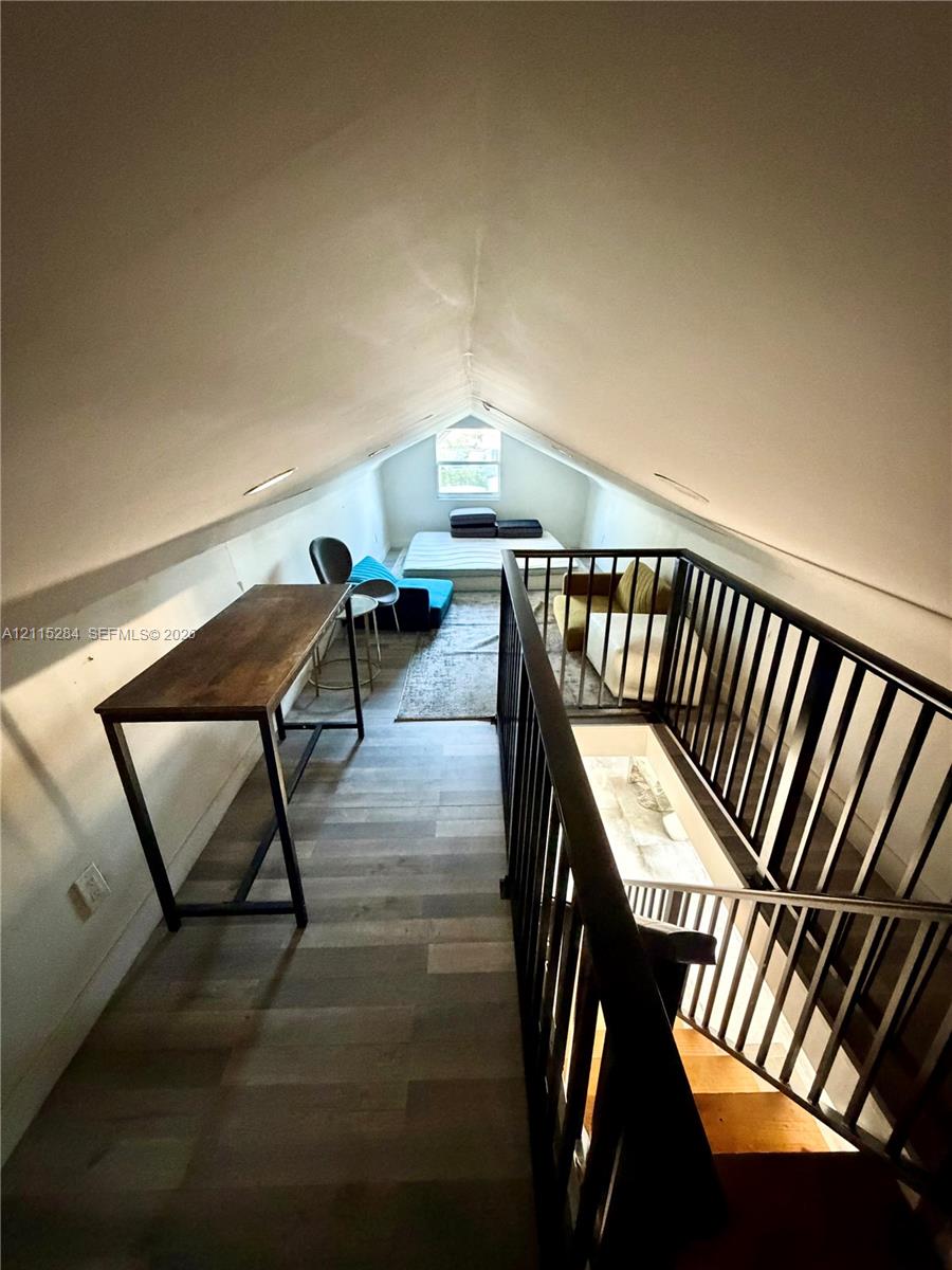 Vaulted ceiling featuring a steeply pitched roofline, wood-finish flooring, and a black metal spindle railing