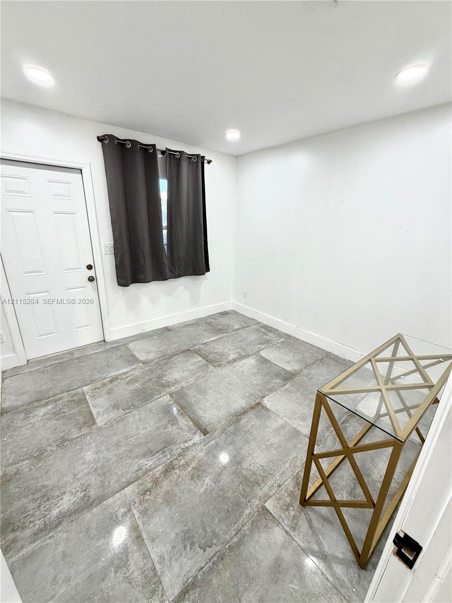 Large-format gray stone-finish floor tiling, recessed ceiling lighting, and a solid-core six-panel door with metallic hardware