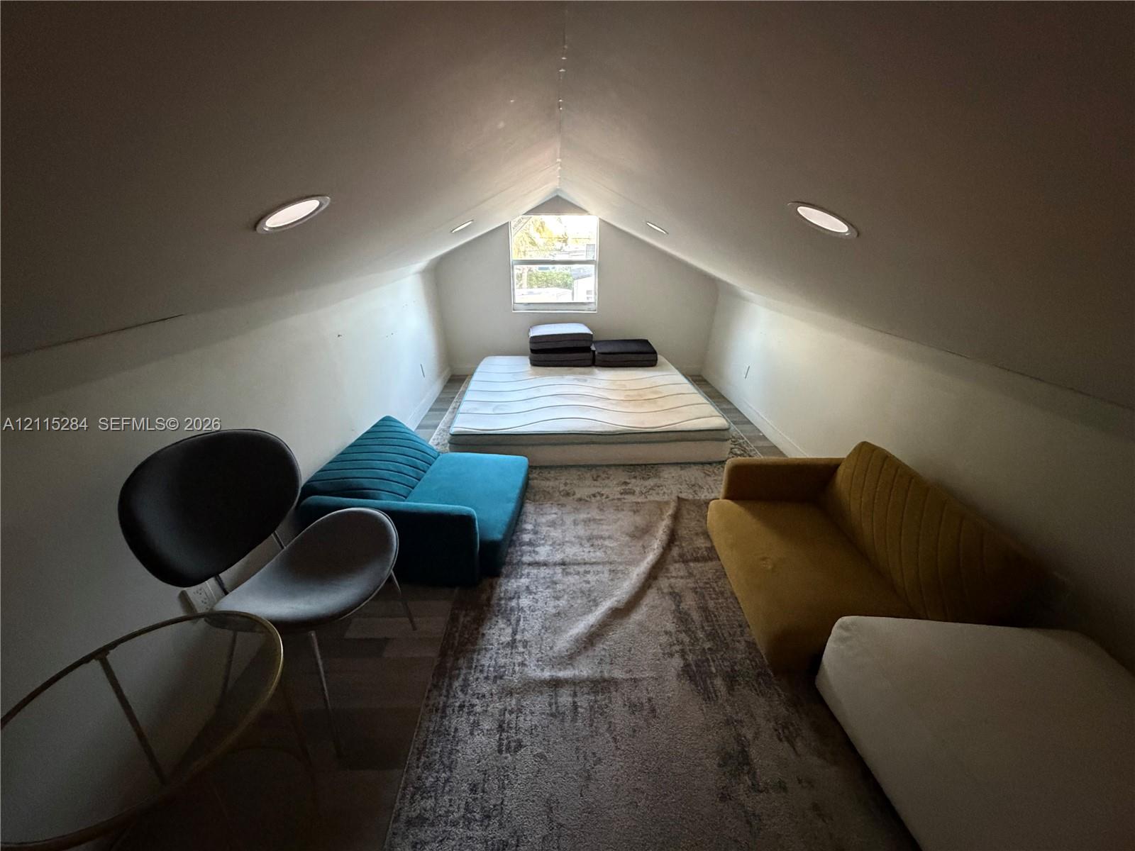 Attic space featuring vaulted ceilings, wood-finish flooring, and recessed lighting
