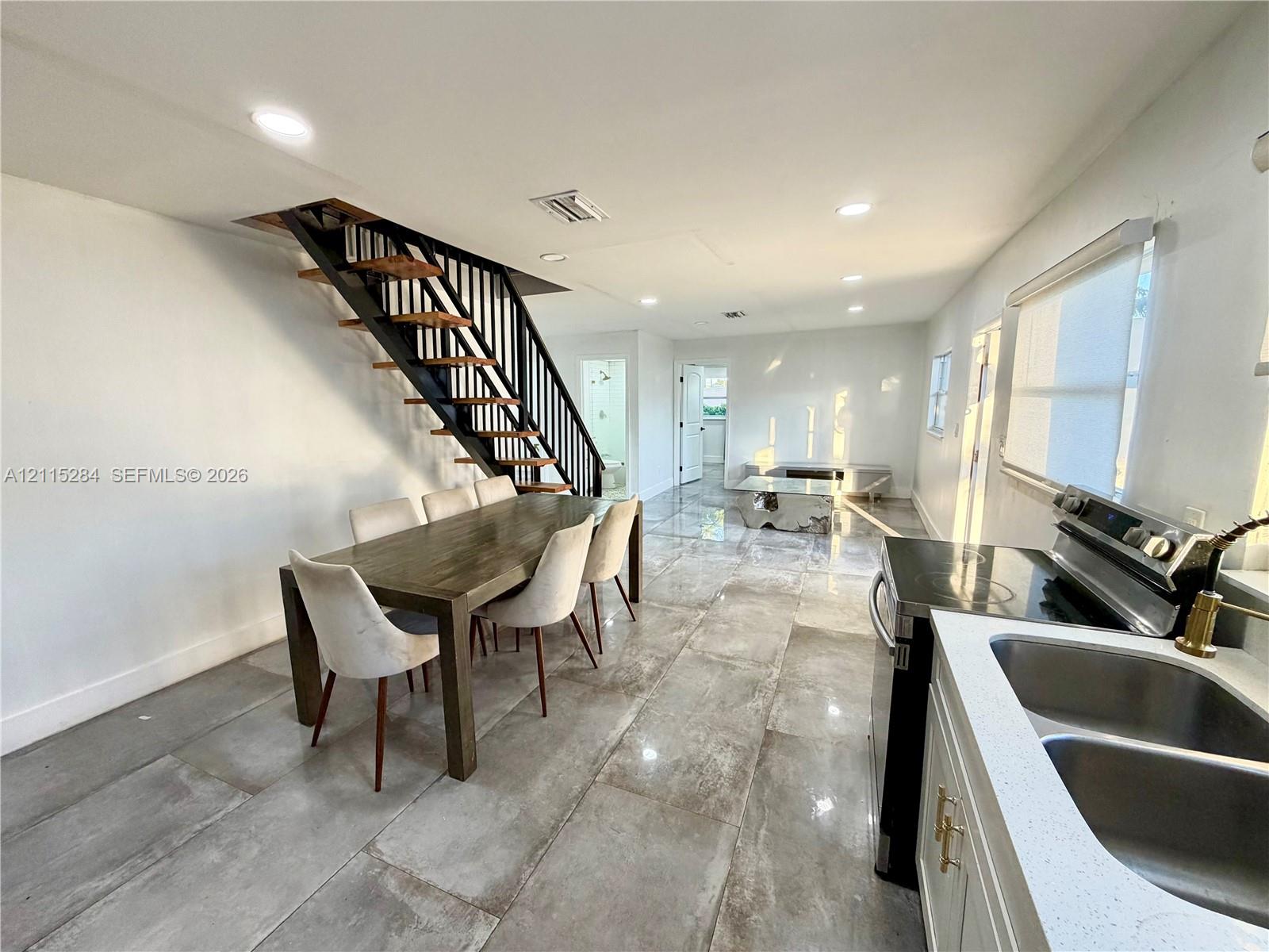 Open-concept interior featuring large-format tile flooring, recessed ceiling lighting, and a floating staircase with dark metal railings