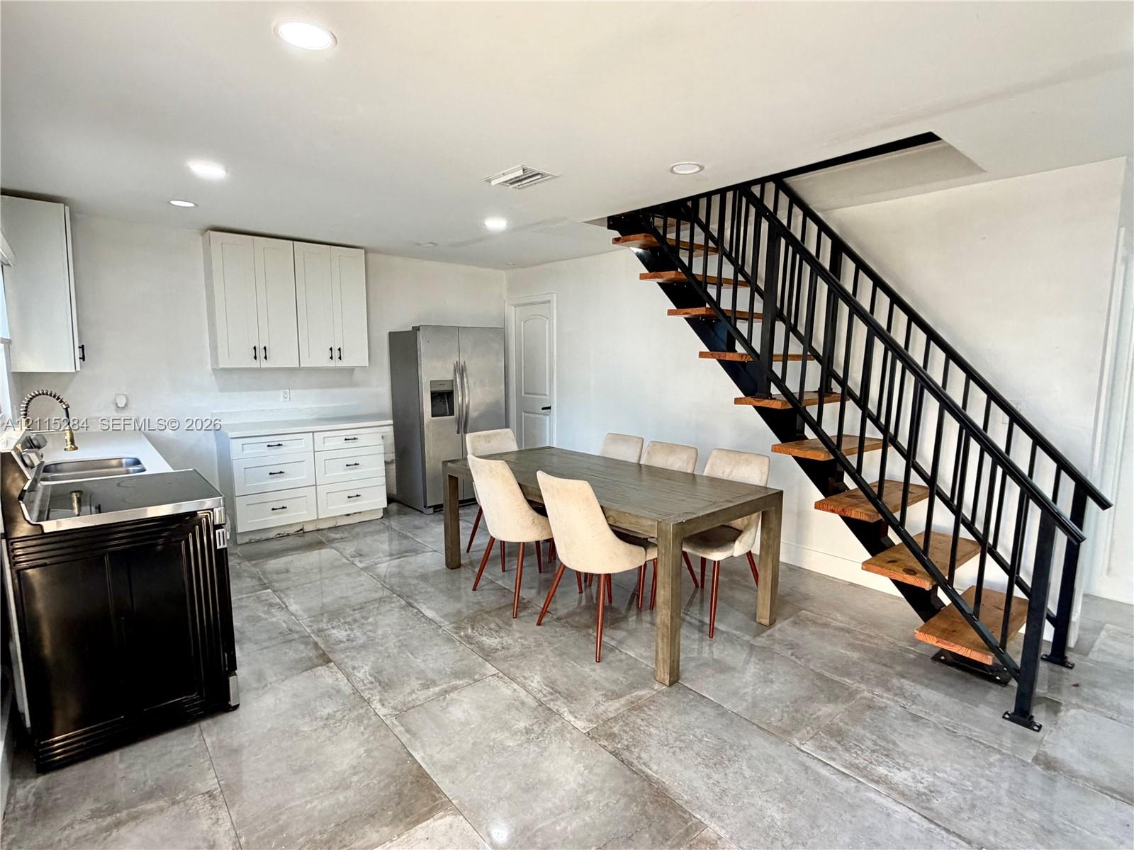 Open-concept interior featuring large-format tile flooring, white shaker-style cabinetry, recessed lighting, and an industrial-style staircase with wood treads and black metal railings