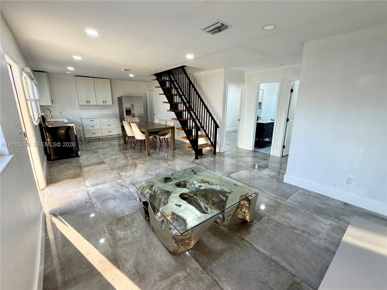 Open-concept interior featuring large-format tile flooring, a metal staircase with wooden treads, recessed lighting, and cabinetry with integrated stainless steel appliances