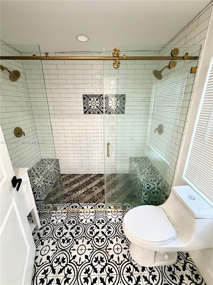 Walk-in shower featuring a brass sliding glass door system, dual shower heads, integrated benches with patterned tile, and white subway tile surround, complemented by patterned floor tile