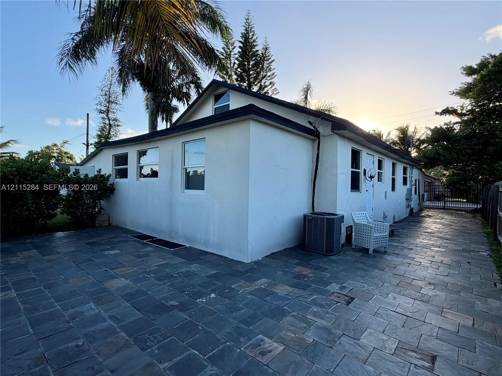 Exterior featuring smooth stucco siding, multi-pane windows, and extensive natural stone paver hardscaping