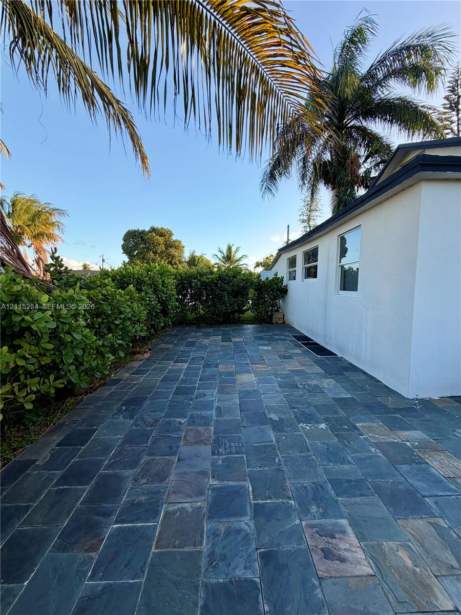 Natural stone paved patio featuring dense perimeter shrubbery and mature palm trees