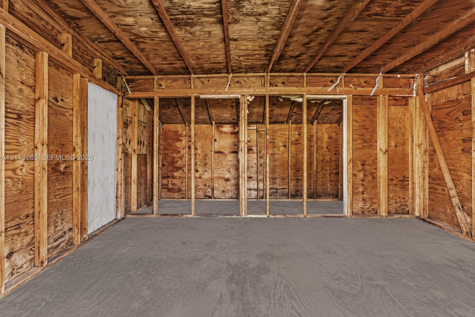 Unfinished space with exposed wood-frame wall studs, plywood wall sheathing, exposed ceiling rafters, and a concrete slab floor