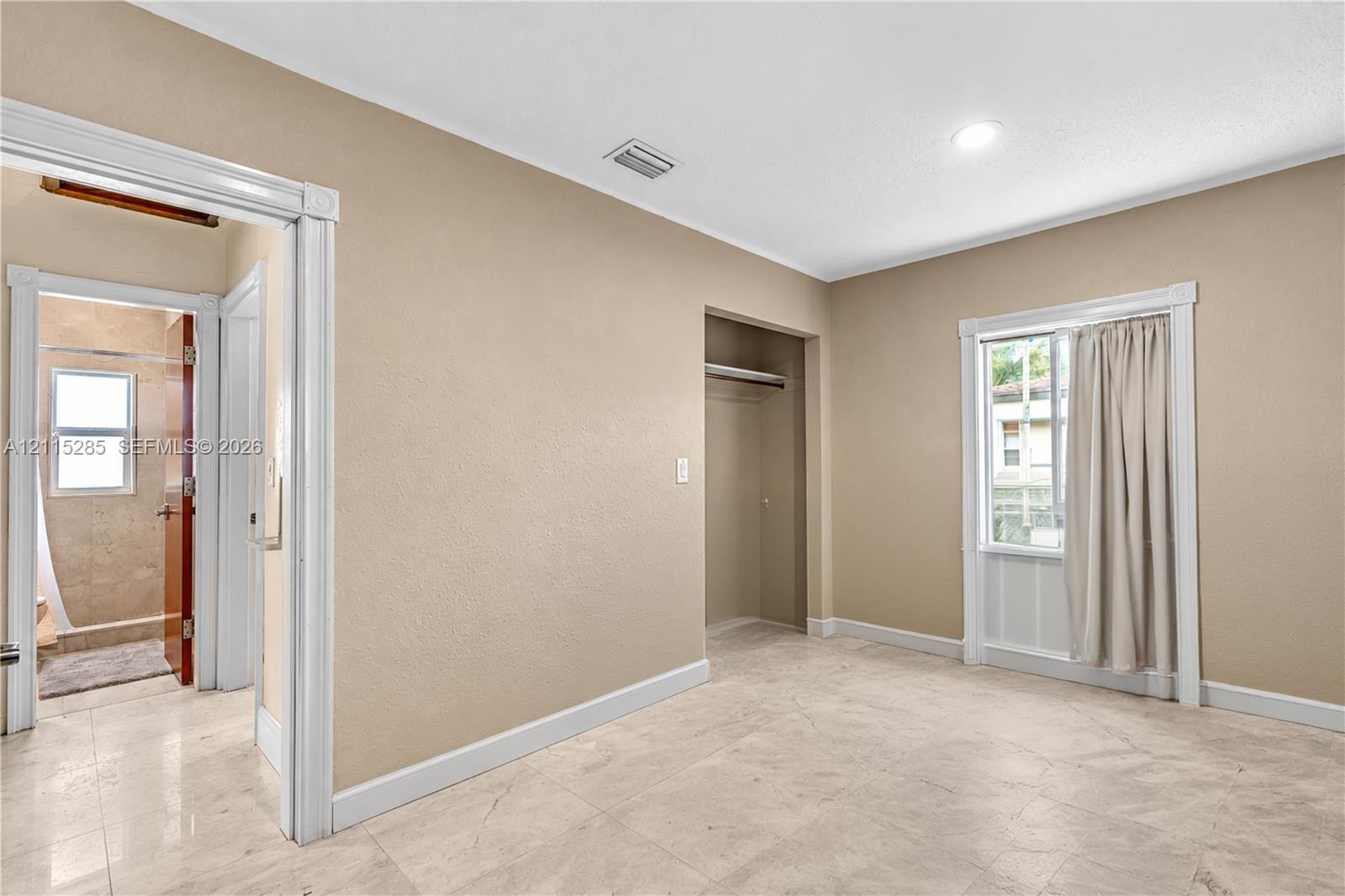 Neutral-toned interior featuring large-format tile flooring, a recessed closet with shelving, and crisp white casing around the window and doorway