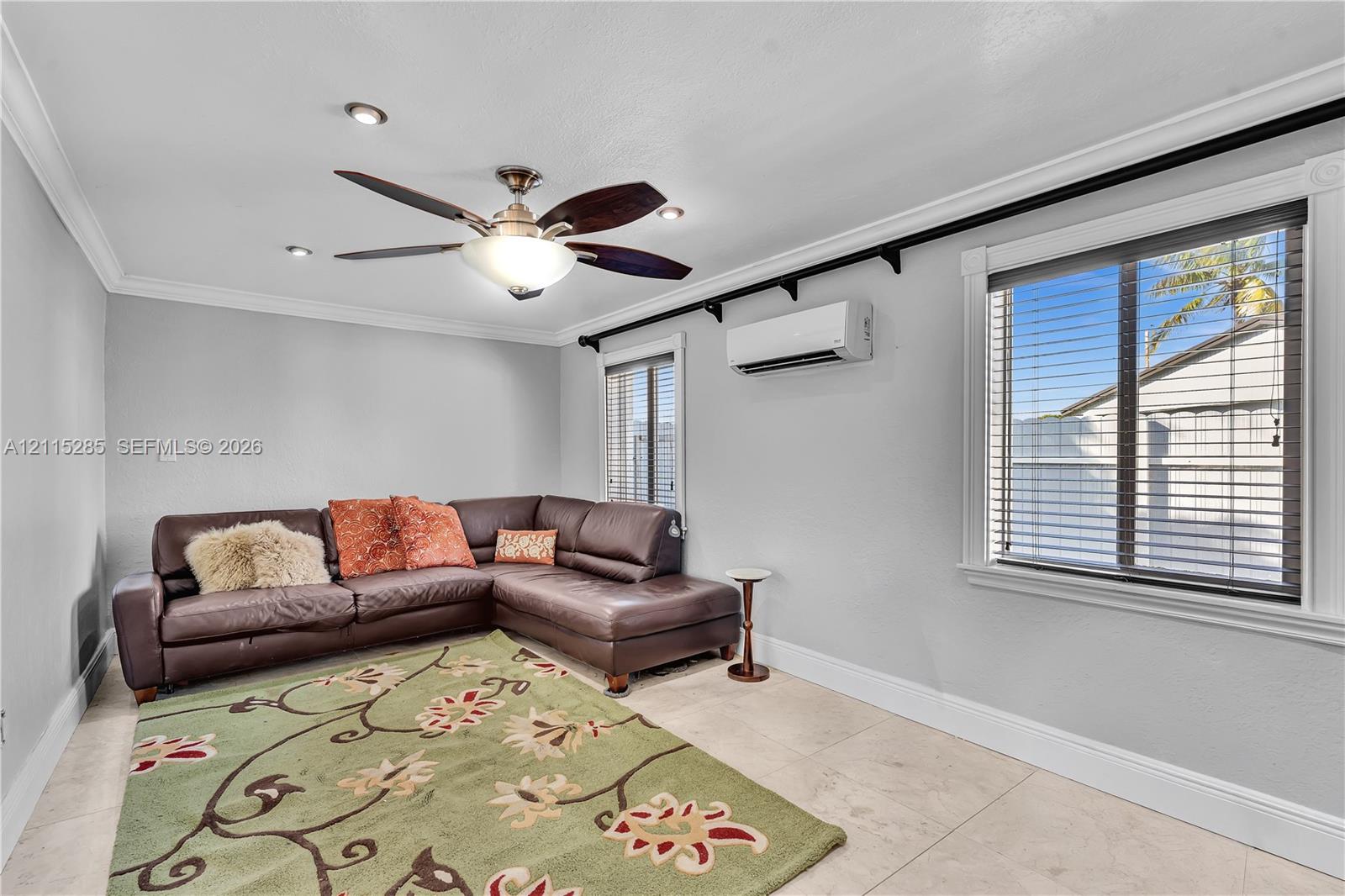 Neutral-toned interior space featuring stone-style tile flooring, crown molding, recessed lighting, a multi-blade ceiling fan, and a wall-mounted ductless climate control unit