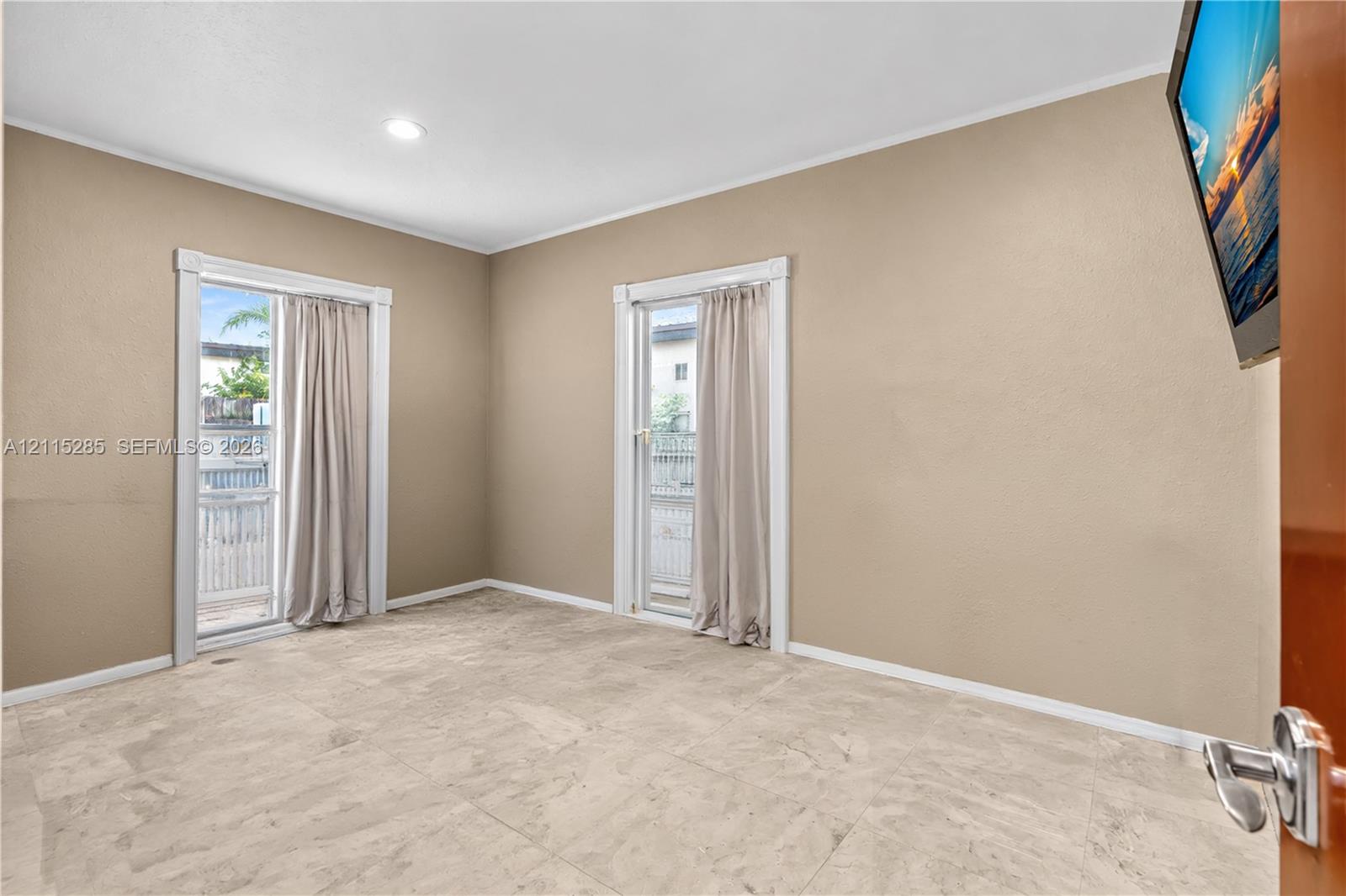 Neutral-toned room featuring large-format tile flooring, recessed ceiling lighting, and two glass-paned doors with white trim