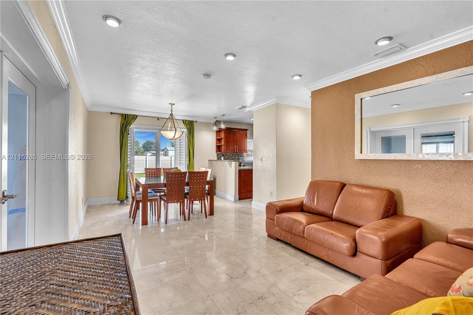 Open-concept interior featuring large-format tile flooring, recessed ceiling lighting, crown molding, and a built-in wall mirror