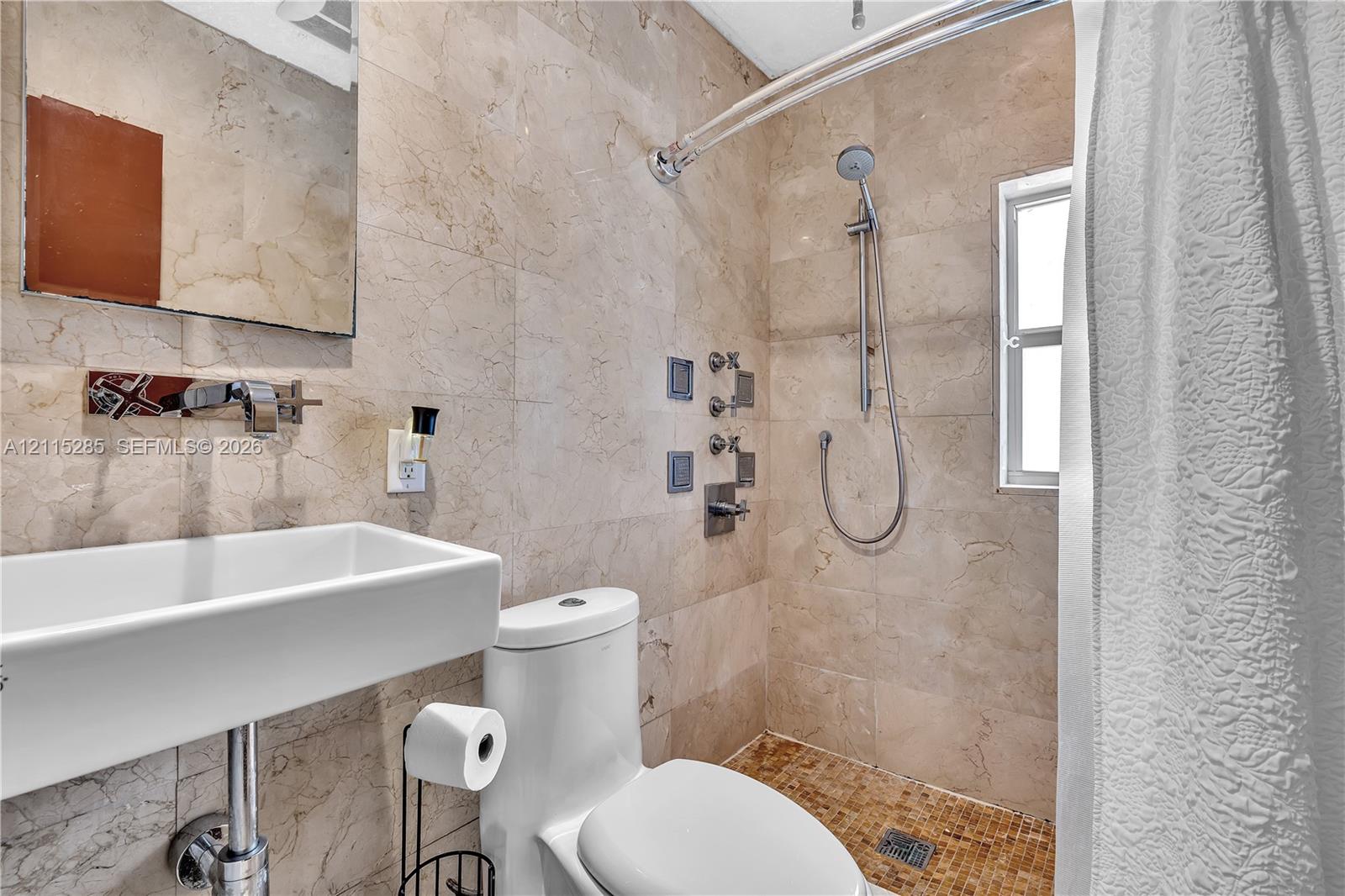 Bathroom featuring stone tile walls, a wall-mounted rectangular vessel sink with a chrome faucet, and a shower system with integrated wall jets and a handheld sprayer